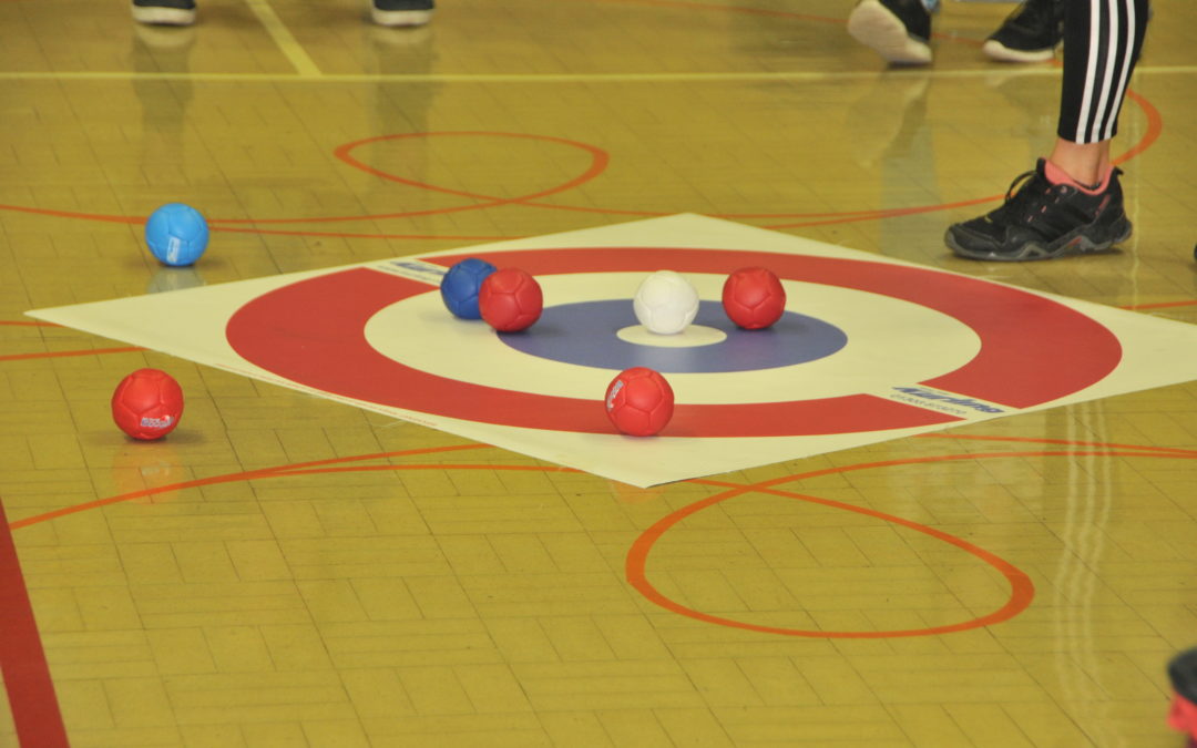 Red and blue boccia balls sit on a target mat during a game.