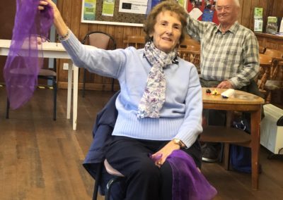 A lady sits on a chair and raises a purple handkerchief upwards