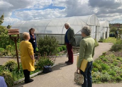 The High Sheriff visits the Active Gardens, he stands and talks to one of the staff members. He is surrounded by plants and behind him are two big poly tunnels