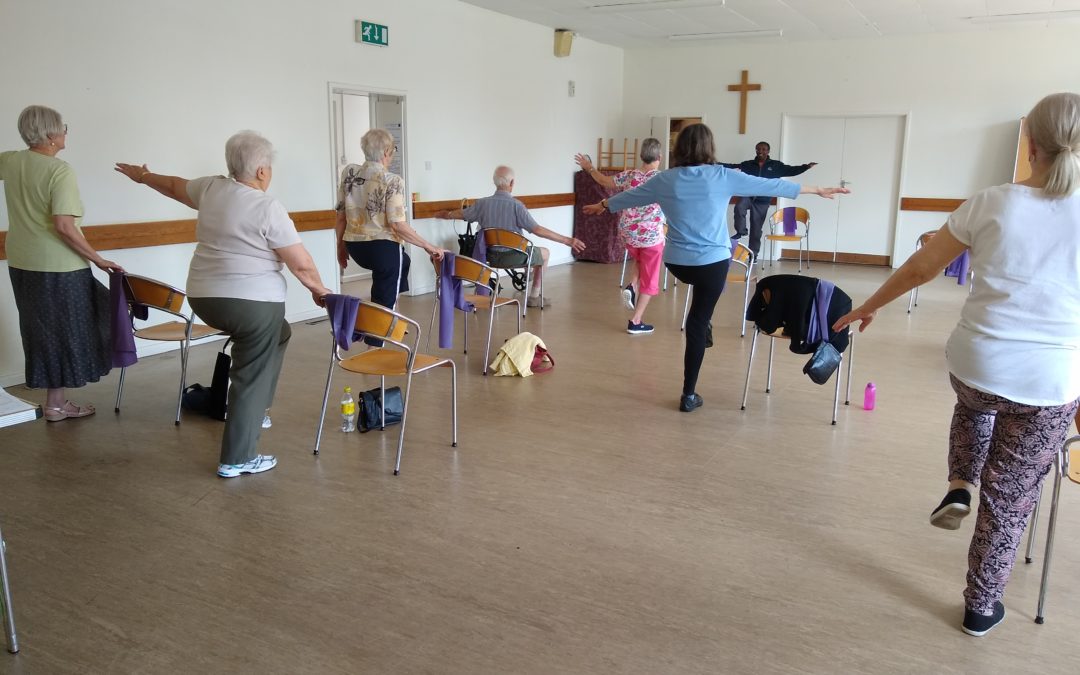 Participants of a Better Balance Class raise their arms and lift one leg off the floor during a Better Balance session