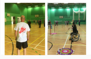 On the left hand side of the image a man stands with his back to the camera wearing a Big Hit t-shirt on the right of the image Donna, a wheelchair user plays badminton