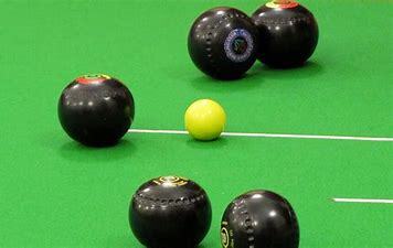 A green bowls court is in the picture as 5 black bowls balls nestle around a yellow jack.