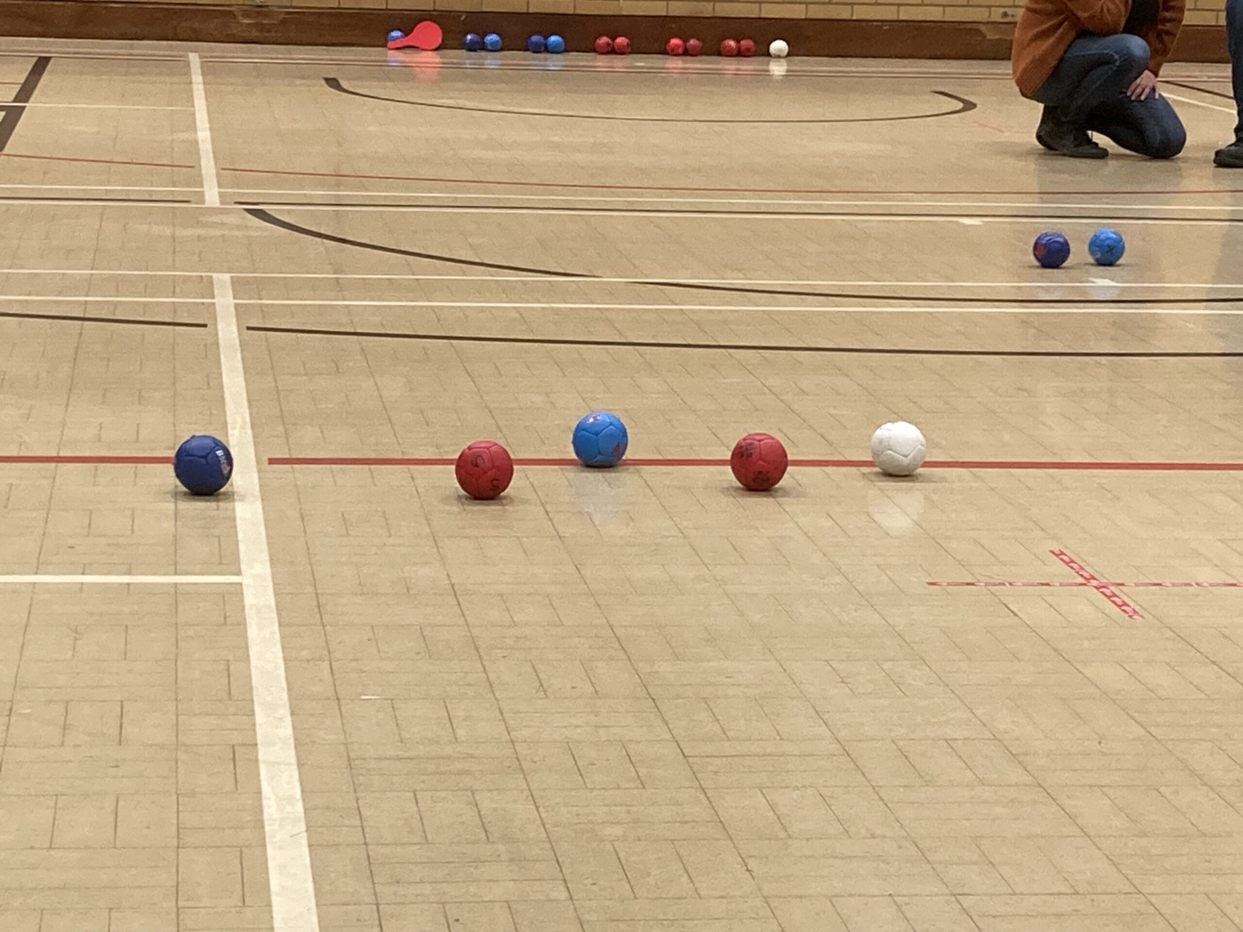 A close up photo of a boccia court. Red and Blue balls surround a white jack ball as a game of boccia progresses.