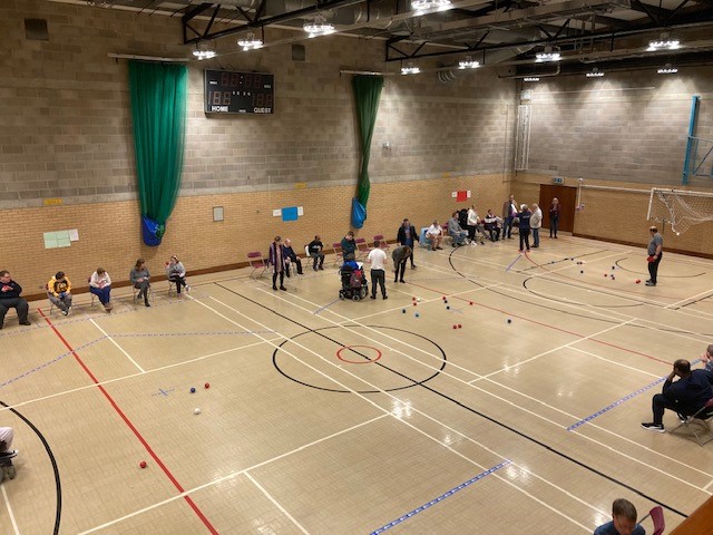 A wide shot of 3 boccia courts all in action during the tournament. Red and Blue balls are being thrown across all of the courts as the games take place.