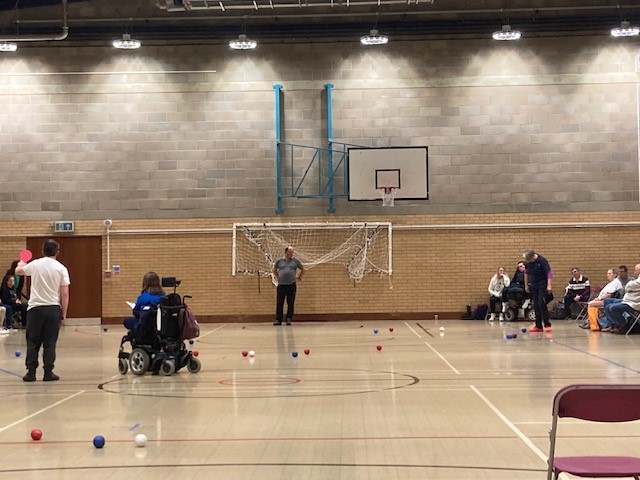 A photo of the boccia courts at the tournament, there are red and blue balls over each of the courts as the games are in progress. You can also see the referees of each game as they mark the scores and ref each game.