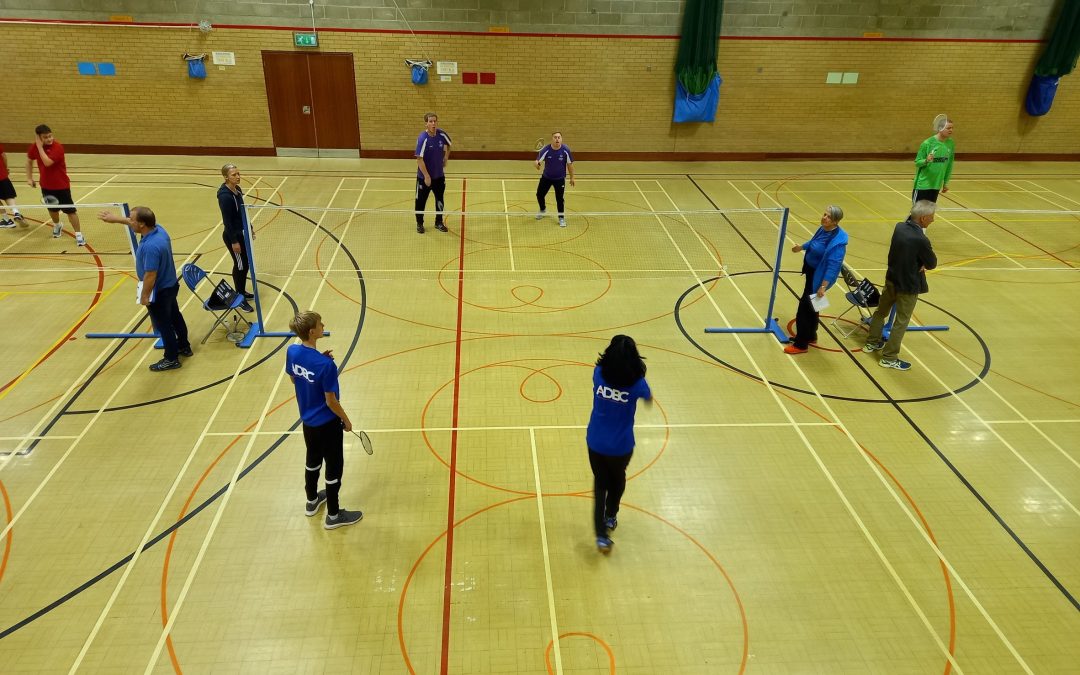 A photo of a badminton court and several players playing a game of badminton.