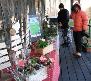 A row of tables can be seen outside the cress pavilion, two people wearing big coats browse the stalls. The stalls are filled with gifts and things to buy.