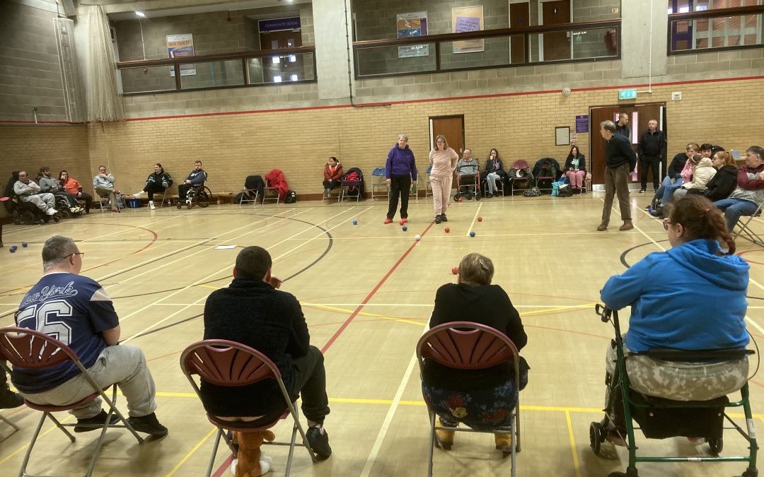 A team of boccia players sit in a row and through their balls onto the court.