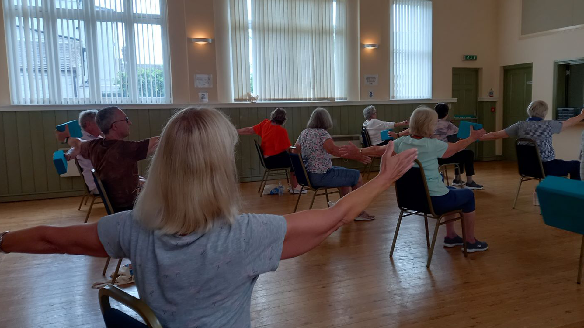 People sit in chairs and swing their arms as they take part in a Better Balance session.