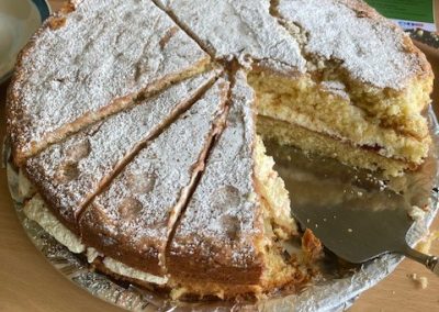 A Victoria sponge cake, several slices have been cut from the cake and a silver cake slice also sits on the cake platter.