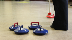 4 blue Kurling irons can be seen on the ground, a person wearing a black pair of trouser and a brush.