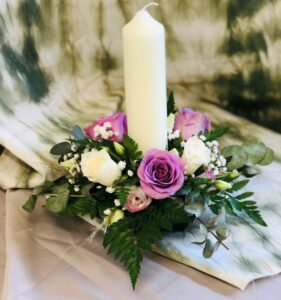 A flower wreath of purple flowers sits around a white candle on a table.