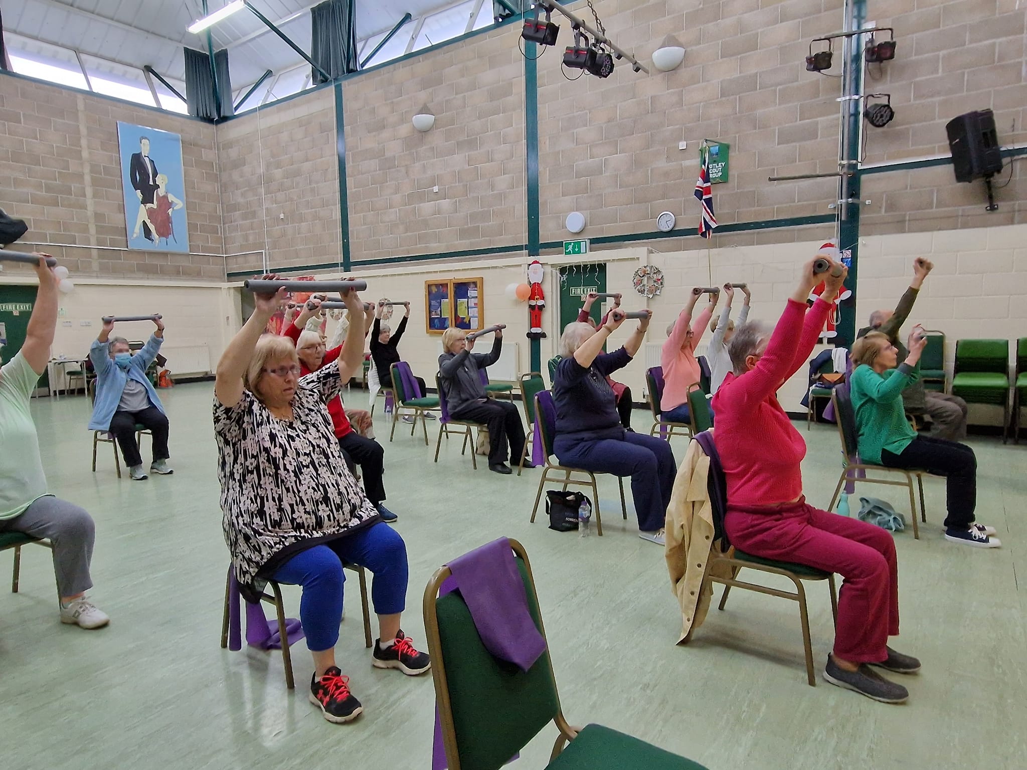 A group of people sit in chairs taking part in a chair based exercise session.