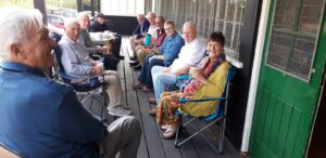 A group of men and a woman sitting on a porch enjoying their drinks and smiling