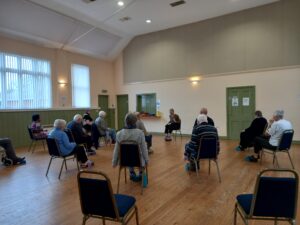 An instructor leading a chair exercise for a group of participants inside a hall