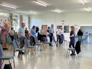A group of participants doing a chair exercise with an instructor leading the session.