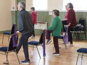 A group of people doing an exercise session using chairs