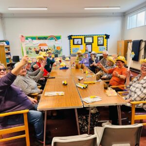 Members of the ActivFriends sitting on a large table, smiling and raising their hands