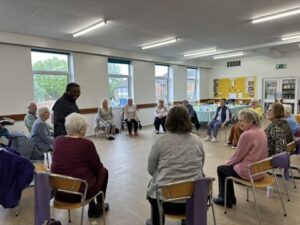 An instructor providing guidance to a group of participants doing a seated exercise