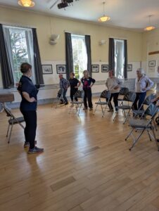AN instructor leading the chair-based exercise with members standing performing a routine.