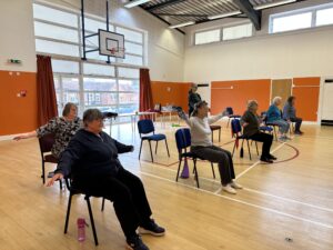 A group of participants doing a seated exercise inside a hall