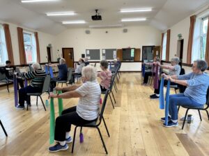 A group of participants doing a seated exercise with an instructor inside a hall