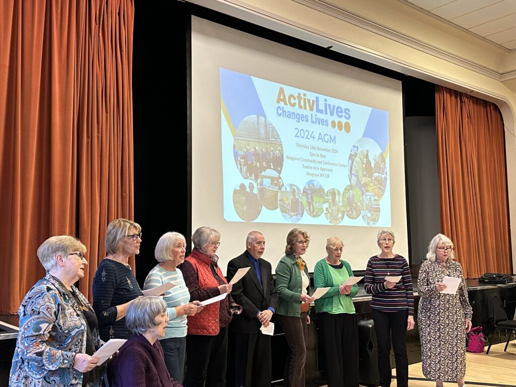 A group of 10 singers serenading the audience during a general meeting of the charity inside an event place.